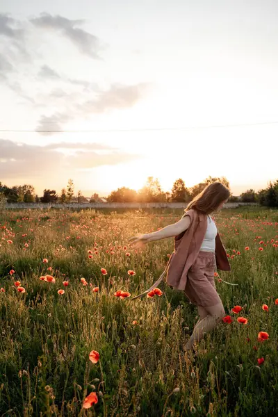 Gün batımında haşhaş tarlasında kahverengi doğal saçlı ve tozlu gül takım elbiseli genç bir kadın. Polonya 'da yaz, Varşova.