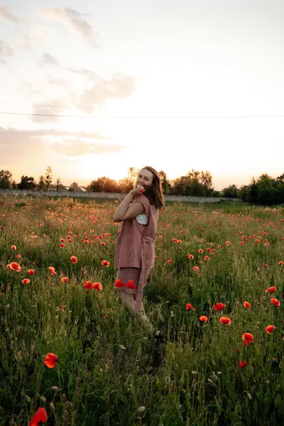Gün batımında haşhaş tarlasında kahverengi doğal saçlı ve tozlu gül takım elbiseli genç bir kadın. Polonya 'da yaz, Varşova.
