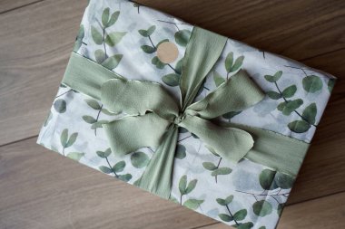 Okaliptüs ve yeşil kurdeleli bir kağıda sarılmış güzel bir hediye. Beyaz arka planda yeşil okaliptüslü ambalaj kağıdı.