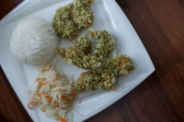 Karides tempura, pirinç, lahana ve havuç salatası. Ahşap masada beyaz tabakta Asya yemeği. Varşova, Polonya 'daki Asya Kafesi.