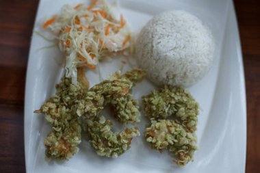 Karides tempura, pirinç, lahana ve havuç salatası. Ahşap masada beyaz tabakta Asya yemeği. Varşova, Polonya 'daki Asya Kafesi.