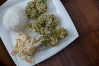 Karides tempura, pirinç, lahana ve havuç salatası. Ahşap masada beyaz tabakta Asya yemeği. Varşova, Polonya 'daki Asya Kafesi.