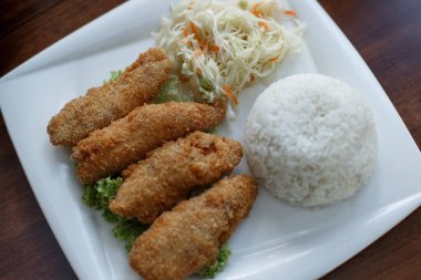 Balık tempura, pirinç, lahana ve havuç salatası. Ahşap masada beyaz tabakta Asya yemeği. Kızarmış balık, pilav ve salata. Varşova, Polonya 'daki Asya Kafesi.