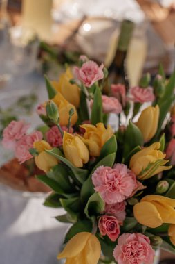 Taze sarı laleler ve pembe karanfiller desenli bir masa üzerinde güneş ışığında. Parlak bahar çiçekleri kutlama, düğün veya romantik tasarım temaları için mükemmeldir..