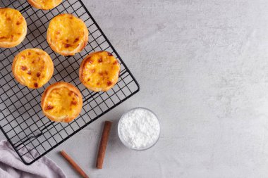 Pastel de Nata yumurtalı tartları, tarafsız gri arka planda metal soğutma rafında dinleniyor. Geleneksel Portekiz tatlısı, altın pullu kabuklu, modern mutfak görselleri için tasarlanmış..
