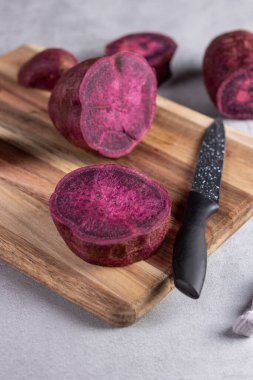  Köy tahtasında siyah bıçakla dilimlenmiş mor tatlı patates. Mor yer elması veya Okinawa tatlı patatesi doğal rengi, sağlıklı beslenmeyi, kök sebzeleri veya doğal besin kavramlarını vurgular.