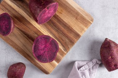 Kırsal ahşap yüzeyde dilimlenmiş mor tatlı patates. Okinawa kök sebzesinin yatay fotoğrafı canlı renkleri, doğal dokuyu ön plana çıkarır ve sağlıklı yiyecekleri ve temiz yemek temalarını destekler.