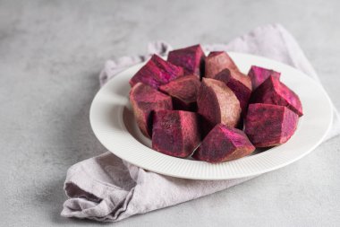 Seramik tabakta yumuşak gri arkaplanlı tatlı patates dilimleri. Minimum düzen bitki temelli diyet, sağlık temaları ve kök sebzeli modern gıda tasarımı destekliyor