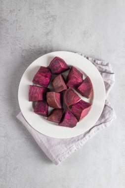 Mor yer elmasının düz yatağı mermilere bölünmüş, beyaz plaka üzerine nötr arkaplan üzerine yerleştirilmiş. Temiz yemek fotoğrafı doğal beslenmeye, sebze konseptine ve sağlıklı yaşam tarzına uyuyor..