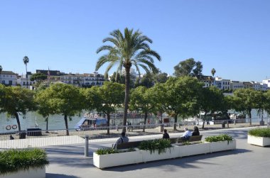 Seville, İspanya - 25 Kasım 2023: Seville, İspanya 'daki Triana mahallesine manzaralı Guadalquivir nehri boyunca yürüme bankı.