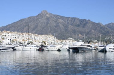 Marbella, İspanya - 10 Aralık 2023: Marbella, Endülüs, İspanya 'daki Dağın eteğindeki Port Banus' ta beyaz tekne ve evler.