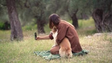 Bir kadın, neşeli köpeğiyle Alacakaranlık 'taki yeşil zeytin koruluğunda selfie anı yakalar. Galli Corgi Pembroke 'lu kız