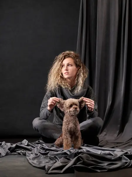 Woman and Poodle share a moment, Indoor bonding captured. A contemplative woman gently holds the ears of a Poodle, both appearing deep in thought, in a tranquil studio setting