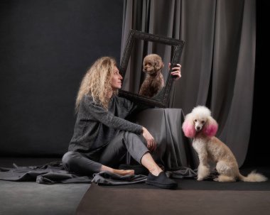 Bir kadın süslü bir çerçevenin içinden fino köpeğiyle oynaşmaktan zevk alır, bağlantıları bir stüdyo ortamında garip bir dokunuşla vurgulanır.