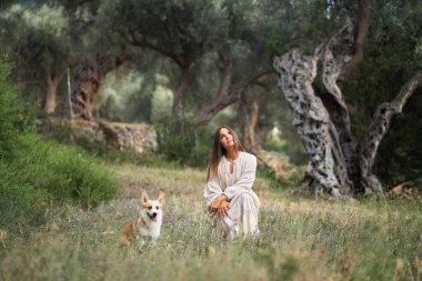 A serene moment unfolds as a woman enjoys playtime with joyful dog Welsh Corgi Pembroke in a lush grove clipart