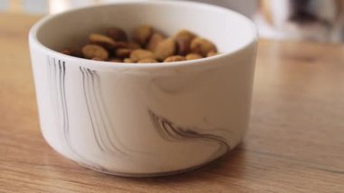 Tahta bir masaya konmuş bir kase köpek mamasının yakın çekimi. Sahne basit, yemek için hazır olan kaseye odaklan..