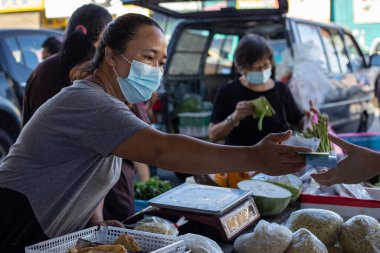 Kota Kinabalu, Sabah, Malezya - 7 Ağustos 2021: Pandemic Covid-19 sırasında yerel malzemelerde yüz maskesi takan alıcının ve satıcının resmi