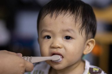 Annenin ellerinin yakın çekimi sabah küçük oğlunun ilk dişlerini temizler. Annem silikon parmak ucu diş fırçasıyla dişlerini fırçalıyor.