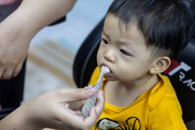 Annenin ellerinin yakın çekimi sabah küçük oğlunun ilk dişlerini temizler. Annem silikon parmak ucu diş fırçasıyla dişlerini fırçalıyor.