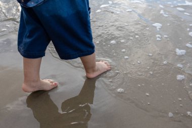 little boy playing with small water on the sand beach.