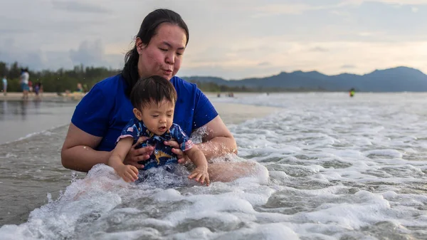 Asian Chinese mother with Happy 1 to 2 years old child enjoying playing on beach with splashing warm sea water