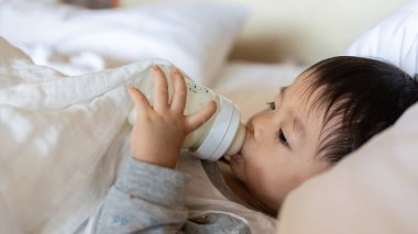 Asian Chinese baby boy age 1 to 2 drinking milk with holding milk bottle by him self.