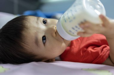 Portrait image of 1 to 2 years old child lying on bed with holding a milk bottle drinking milk
