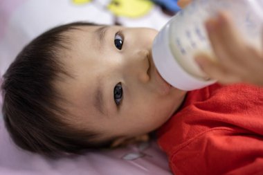 Portrait image of 1 to 2 years old child lying on bed with holding a milk bottle drinking milk
