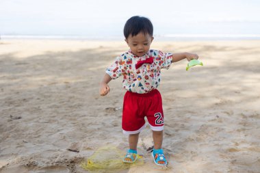 Kumsalda kumsalda oyuncaklarla oynayan Asyalı bir Çinli bebek. Çocuk oyunları. Kumsalda oyunlar