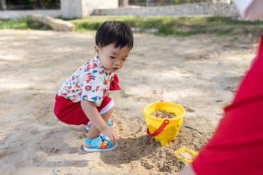 Kumsalda kumsalda oyuncaklarla oynayan Asyalı bir Çinli bebek. Çocuk oyunları. Kumsalda oyunlar