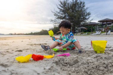 Mutlu 1-2 yaşındaki bir çocuk sıcak deniz suyuyla kumsalda oynamaktan zevk alıyor.