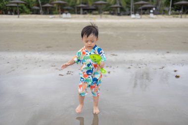 Mutlu 1-2 yaşındaki bir çocuk sıcak deniz suyuyla kumsalda oynamaktan zevk alıyor.