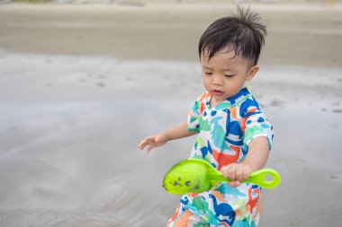Mutlu 1-2 yaşındaki bir çocuk sıcak deniz suyuyla kumsalda oynamaktan zevk alıyor.