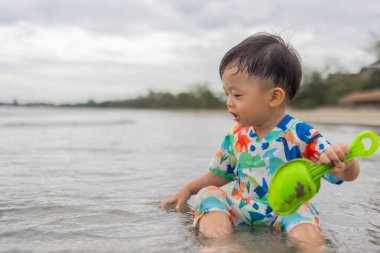 Mutlu 1-2 yaşındaki bir çocuk sıcak deniz suyuyla kumsalda oynamaktan zevk alıyor.