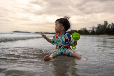 Mutlu 1-2 yaşındaki bir çocuk sıcak deniz suyuyla kumsalda oynamaktan zevk alıyor.