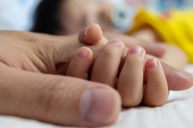 Bebek uyurken babanın elini tutan bir bebek. Babası oğluyla ilgileniyor. Mutlu aile sağlık hayali kuruyor.