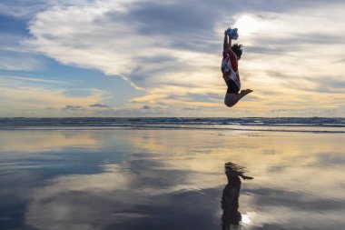 Mutlu bir bayan, güzel bir alacakaranlık günbatımında Kudat, Sabah, Borneo sahillerinde mutlu bir atlayış yapar.