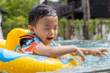 Asyalı bir çocuk mutlu ve çocukların şişme yüzme yüzüğüyle bilardo oynamaktan zevk alıyor.