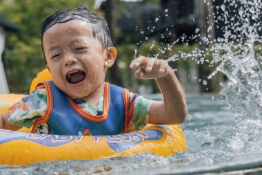 Asyalı bir çocuk mutlu ve çocukların şişme yüzme yüzüğüyle bilardo oynamaktan zevk alıyor.