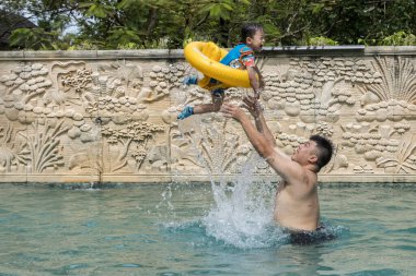 Mutlu Asyalı çocuklar ve babaları havuzda oynuyorlar.
