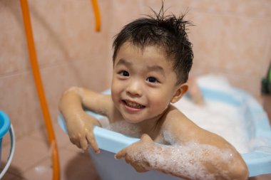 Sevimli ve mutlu erkek bebek banyo yapmaktan ve baloncuk oynamaktan zevk alıyor.