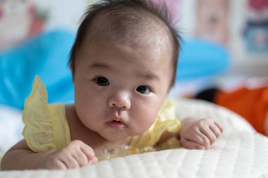 Yatakta yatarken gülümseyen Asyalı Çinli bebek kız. Mutlu yeni doğan çocuk yatakta dinleniyor.