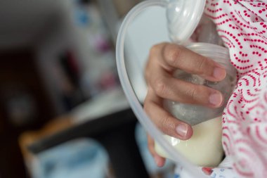 Asyalı Çinli anne yatak odasında bebeğine süt pompalamak için göğüs pompası kullanıyor. Colostrum süt, Geçiş sütü, Meme Pompalama süt konsepti.