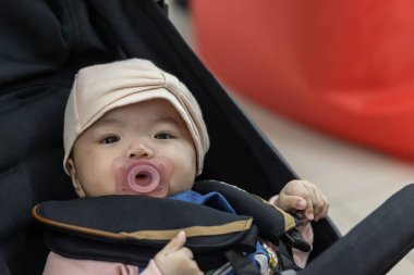 4 aylık Asyalı Çinli Bebek Kız 'ın portresi ağzında emziğiyle Gezginin Konforu' ndan dünyayı keşfediyor.