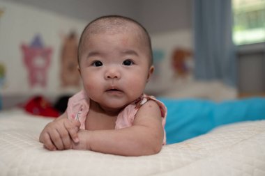 4 aylık Asyalı Çinli bebek kızın yatakta yatarken gülümseyen yüzü. Mutlu yeni doğan çocuk yatakta dinleniyor.