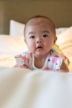 Dağılmış kırmızı gül yapraklarıyla çevrili bir yatakta uzanmış, neşeli bir gülümseme sergileyen sevimli bir bebek.