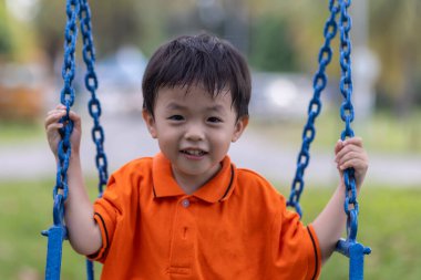 Mutlu genç çocuk güzel bir akşam ışığı olan açık hava parkında salıncaktan hoşlanıyor.