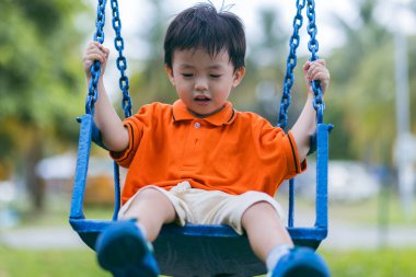 Mutlu genç çocuk güzel bir akşam ışığı olan açık hava parkında salıncaktan hoşlanıyor.