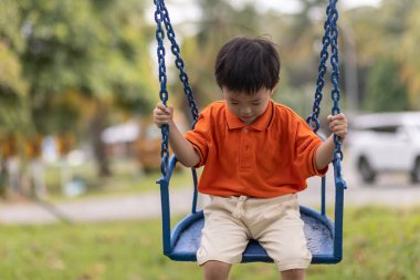 Mutlu genç çocuk güzel bir akşam ışığı olan açık hava parkında salıncaktan hoşlanıyor.