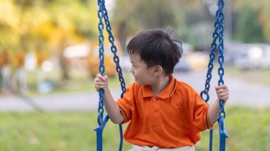 Mutlu genç çocuk güzel bir akşam ışığı olan açık hava parkında salıncaktan hoşlanıyor.